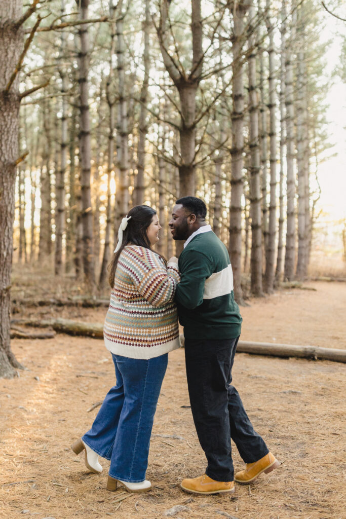 a couple smiling and leaning towards one another during their engagement session in the woods 