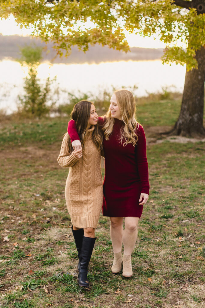 two women walking with their arms around each other next to thew ater 