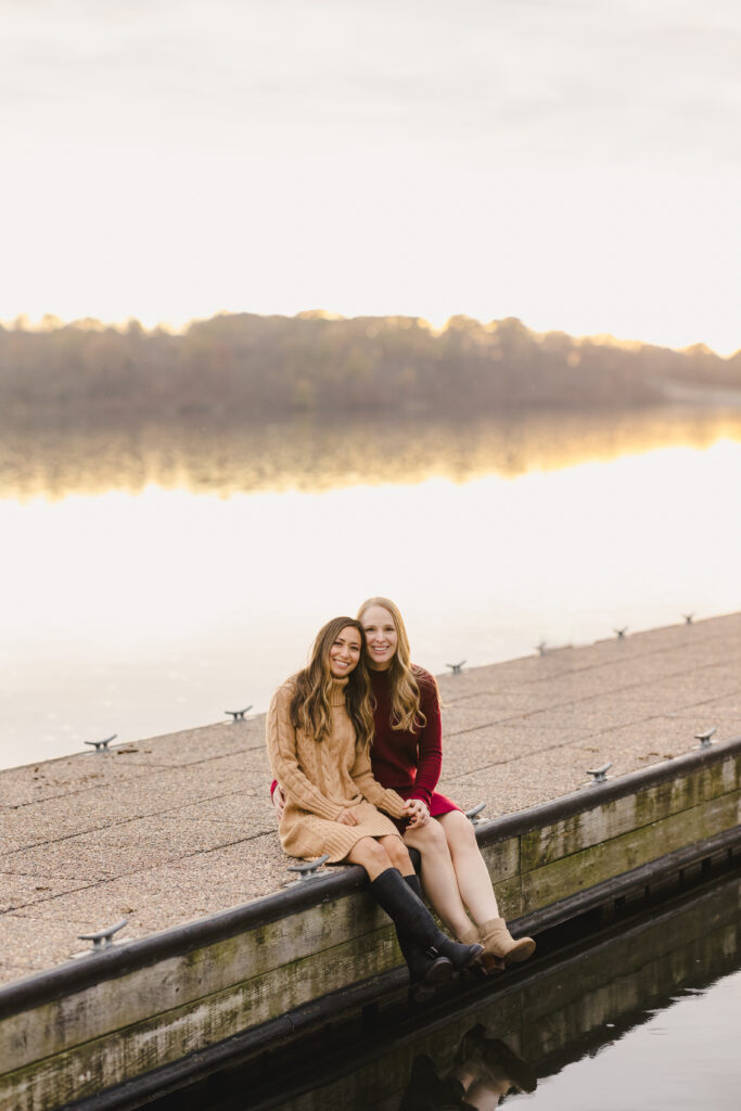 two women sitting together on a dock during their engagement session 
