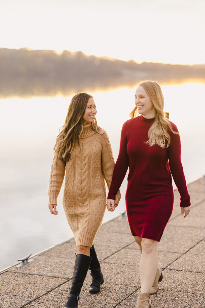 two women walking down a dock holding hands and smiling at each other 