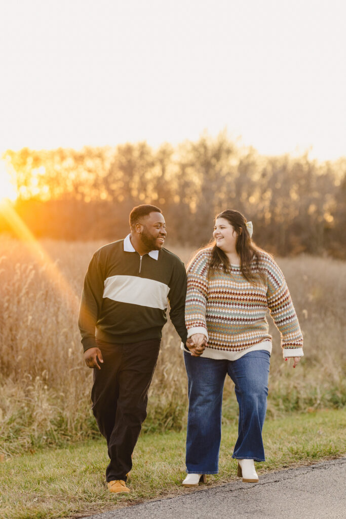 a couple holding hands and walking next to a field 