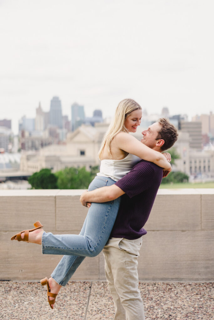 a man picking his partner up on a rooftop in kanasa city during their engagement session 