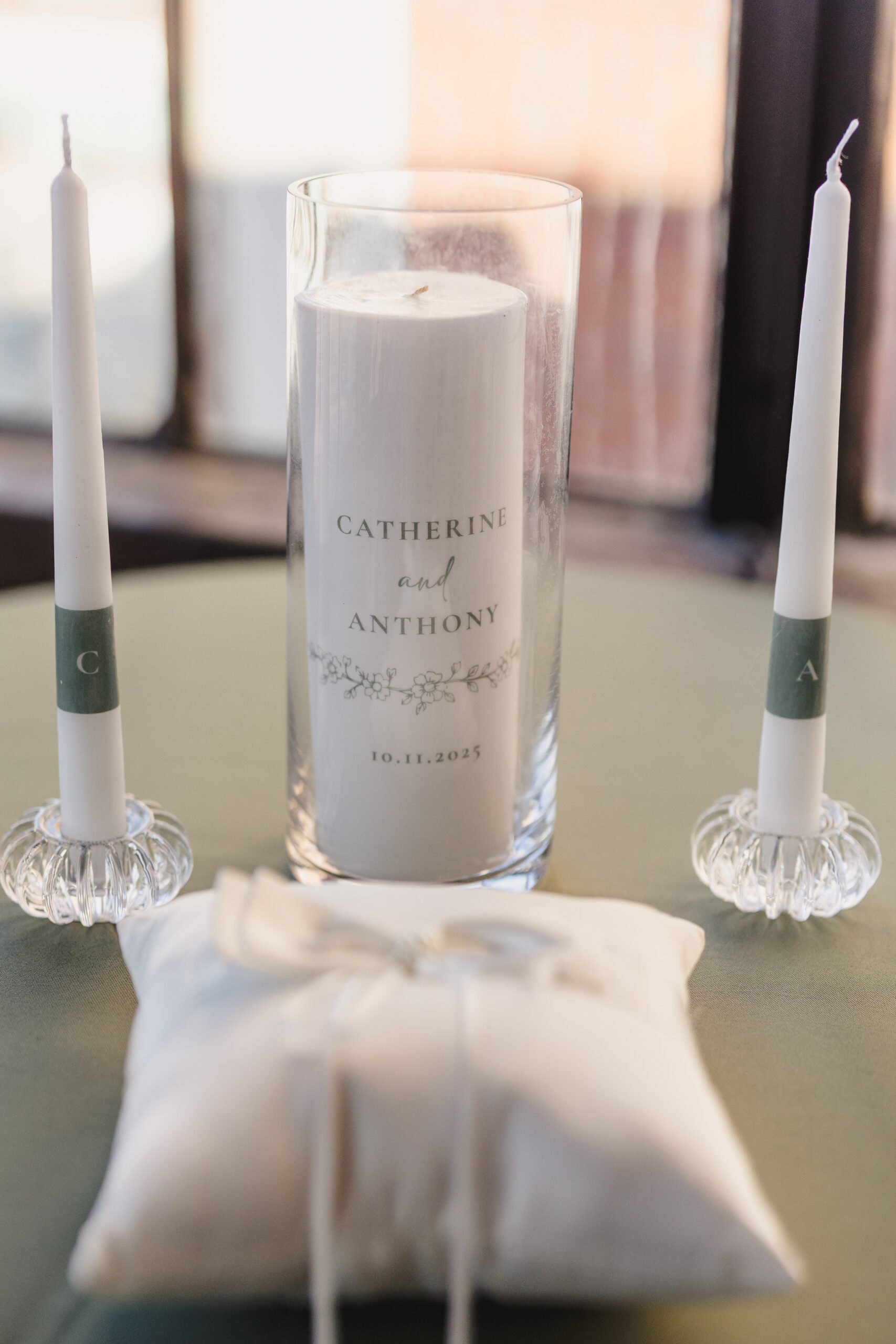 two white candles and an engraved candle on a table set up for a wedding ceremony