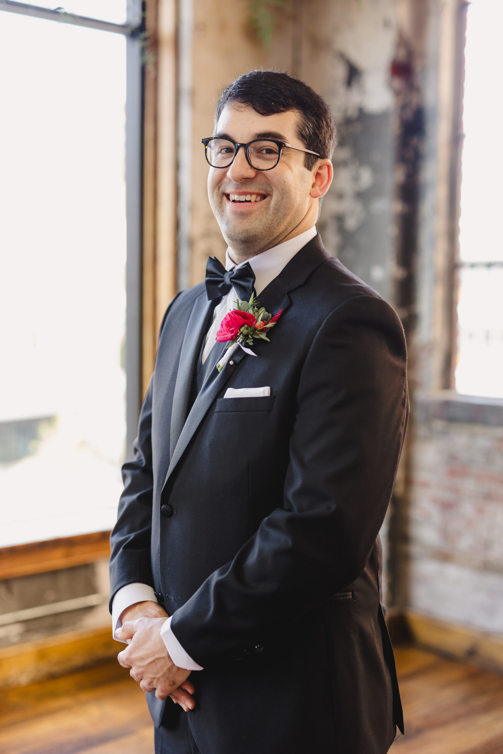 a groom standing with his hands crossed and smiling