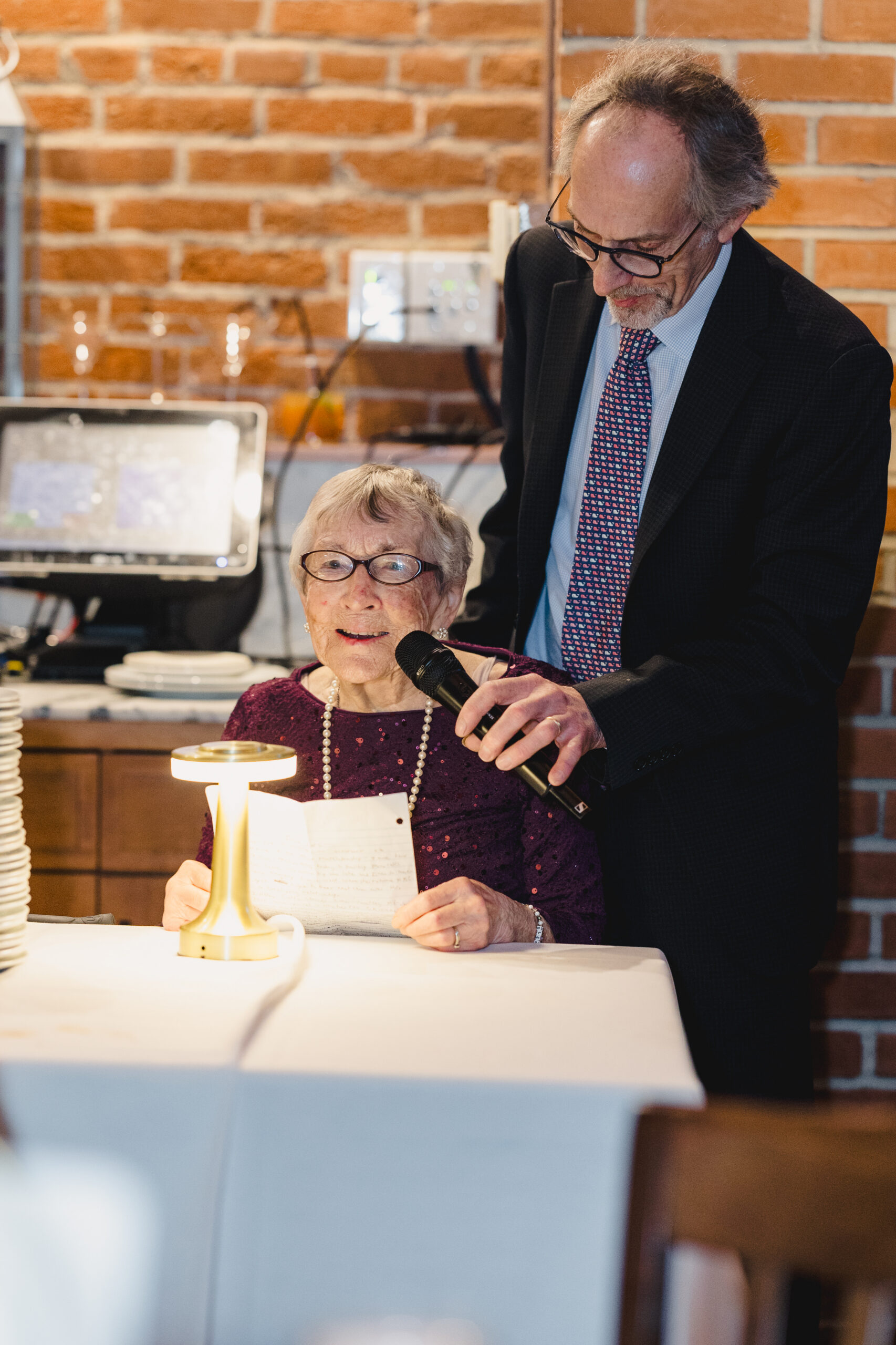 a woman sitting at a table reading a speech at a wedding rehearsal dinner 