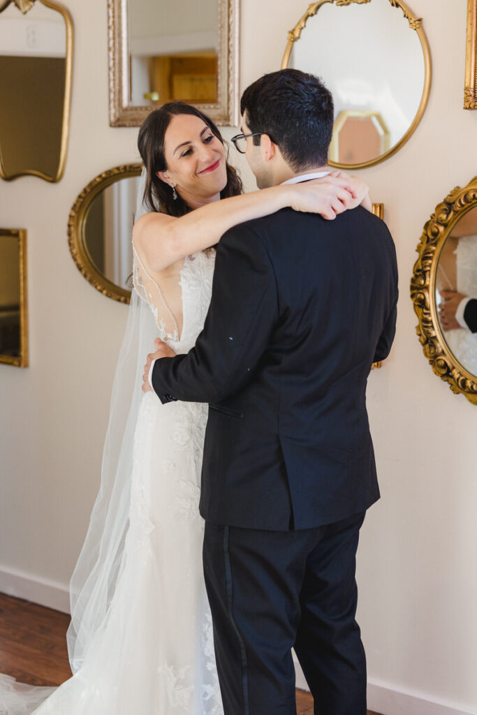 Newlyweds smiling with their arms around each other in front of a wall of mirrors 
