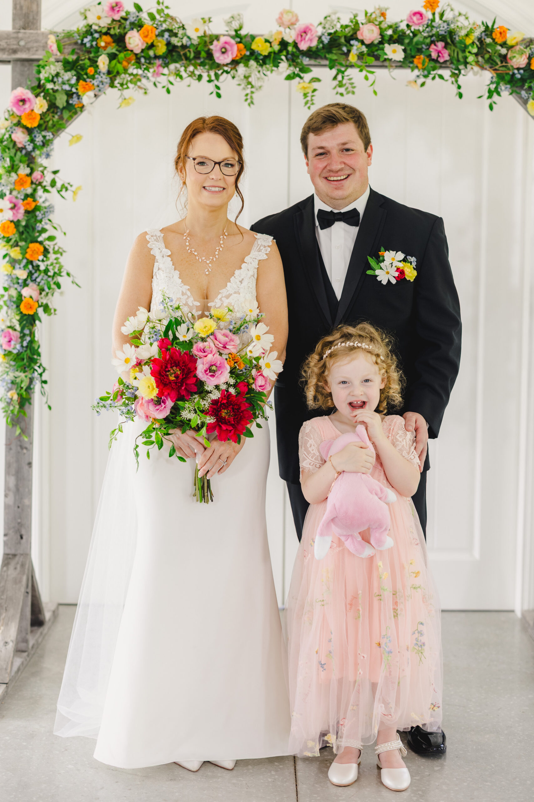a bride and groom with their daughter taking a family wedding photo 