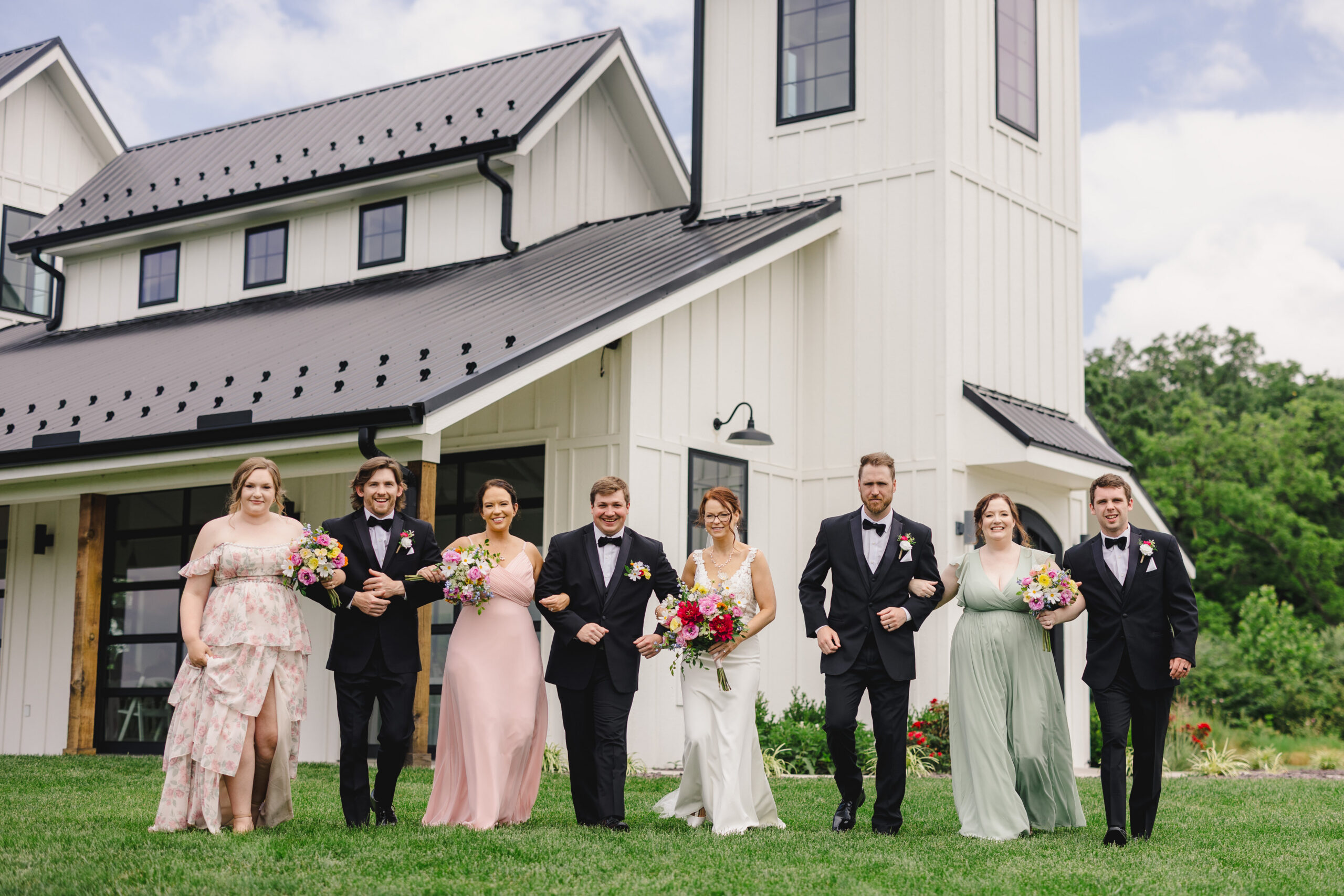 a bride and groom with their wedding party taking photos in the summer in front of the brim in kansas city