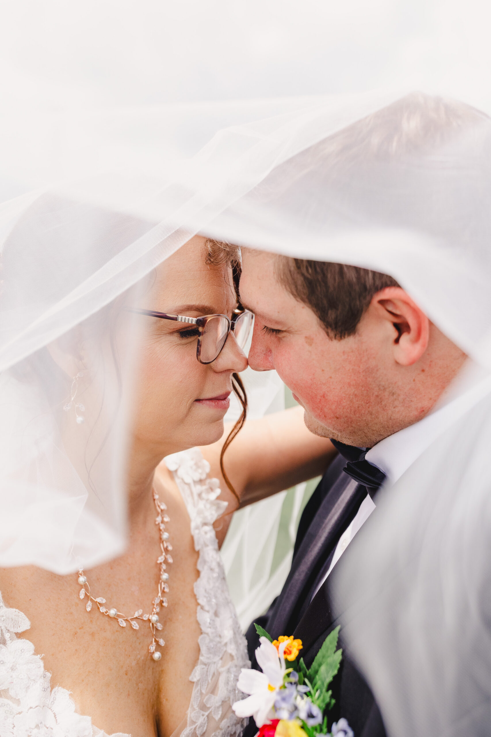 a bride and groom taking wedding portraits underneath the bride's wedding veil