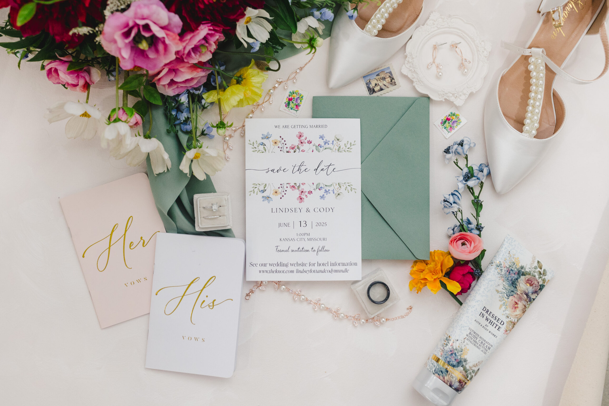 a wedding detail flat lay with wedding invitations, lotions, rings, vow books, and heels 