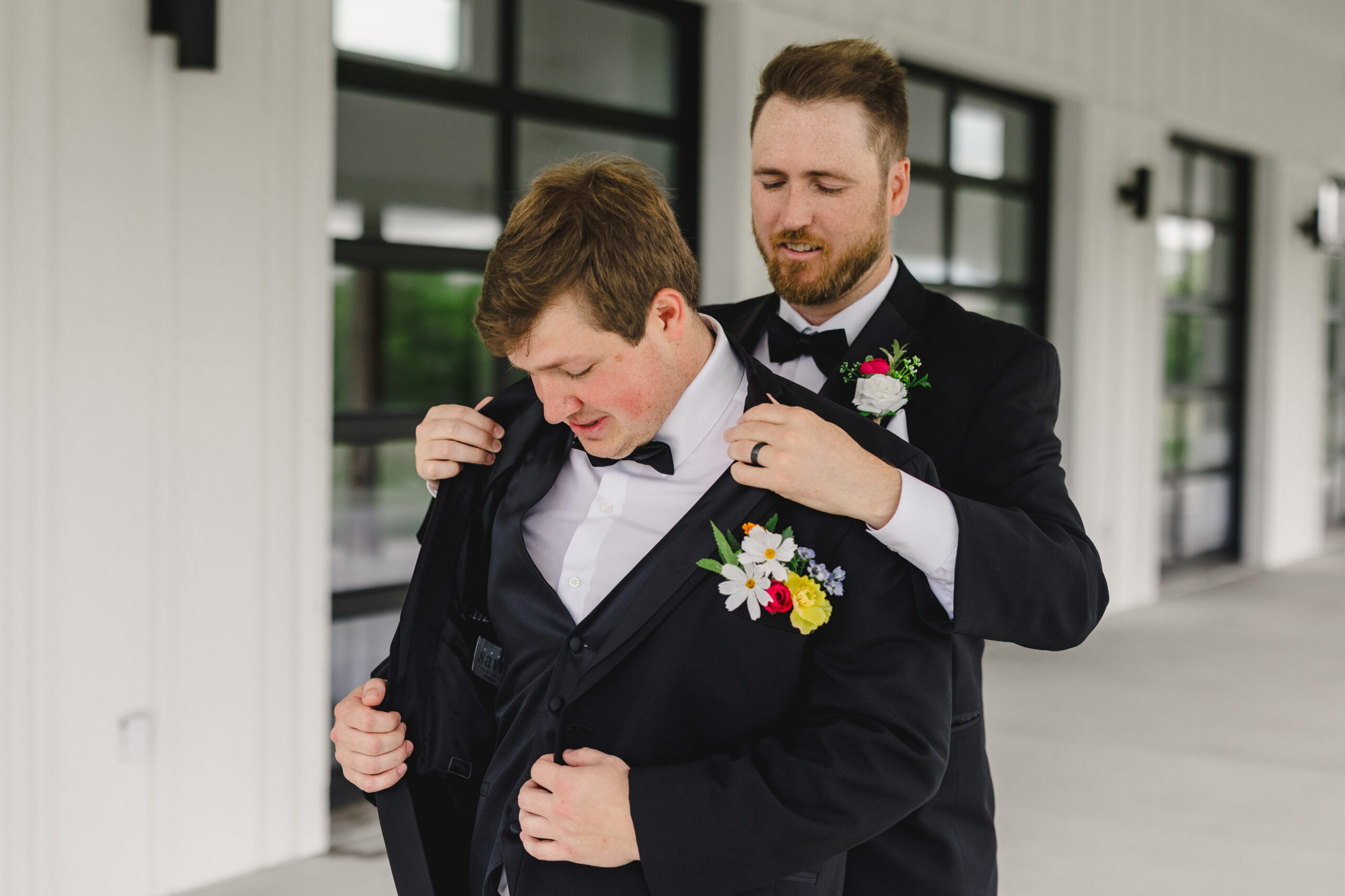 a groomsmen helping the groom put on his suit jacket 