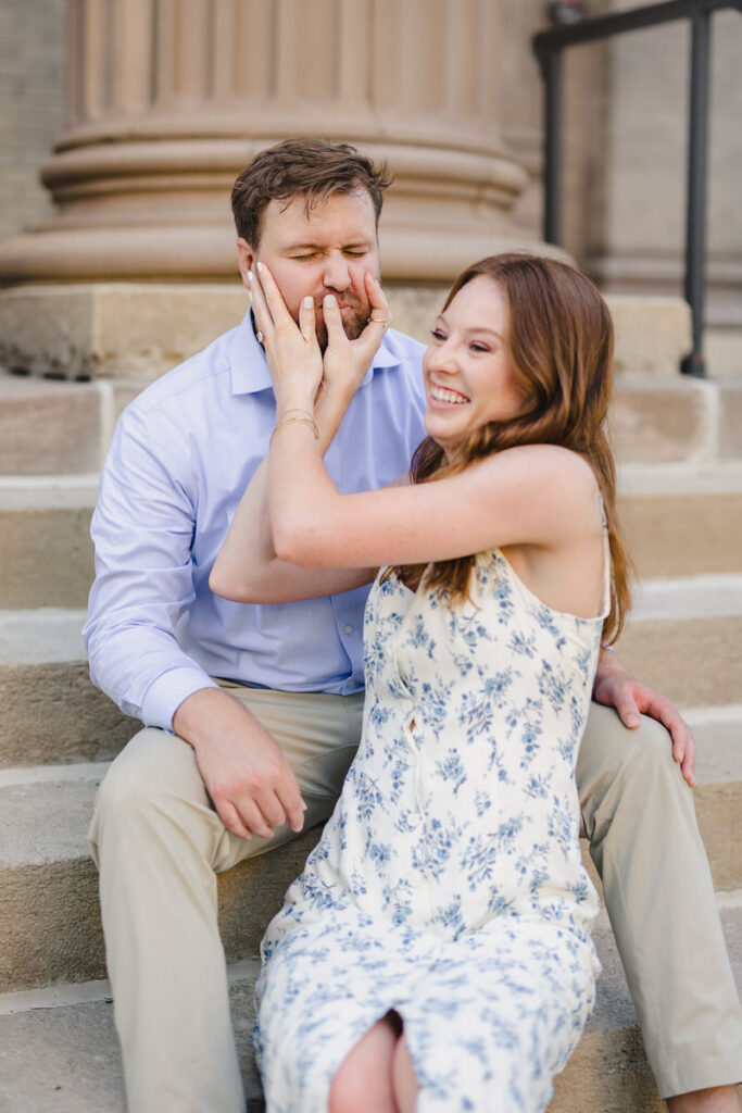 A couple sitting on a staircase as one squeezes the other's cheeks and laughs