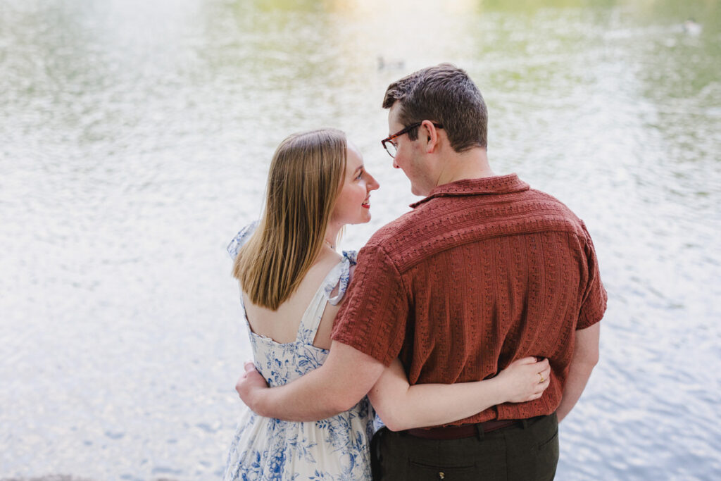 A couple with their arms around each other smiling at each other in front of a lake