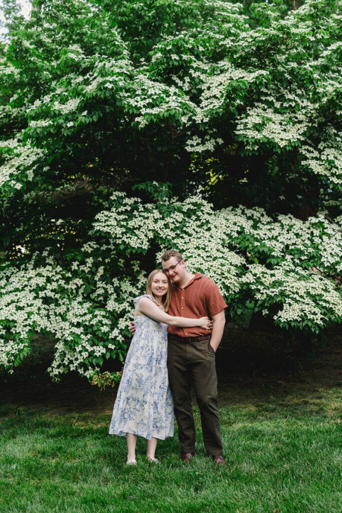 A couple hugging in front of a green and white tree