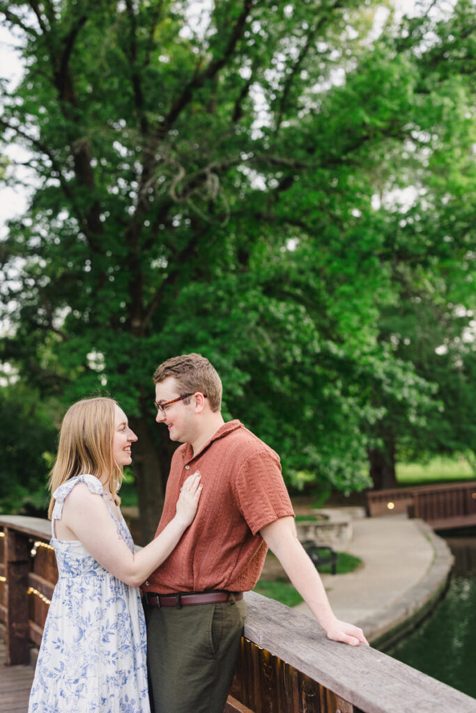 A couple leaning against the railing of a small bridge as one rests their hand on the other's chest
