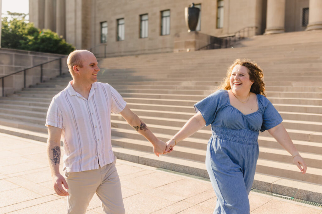 A couple holding hands and walking in front of a staircase to a building
