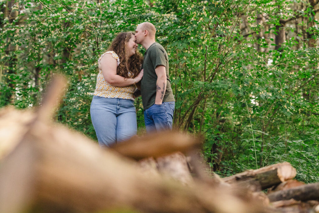 A couple standing close together in the woods as one kisses the other's forehead