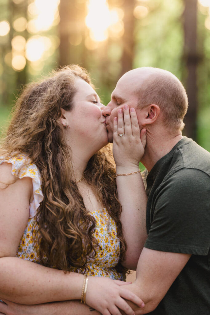 A couple kissing while one has their hand on the other's face showing off an engagement ring