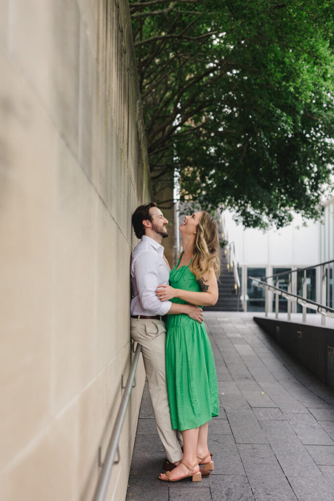 A couple standing close together and laughing while leaning on a building