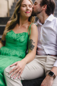 A couple sitting on a staircase together as one kisses the other's cheek