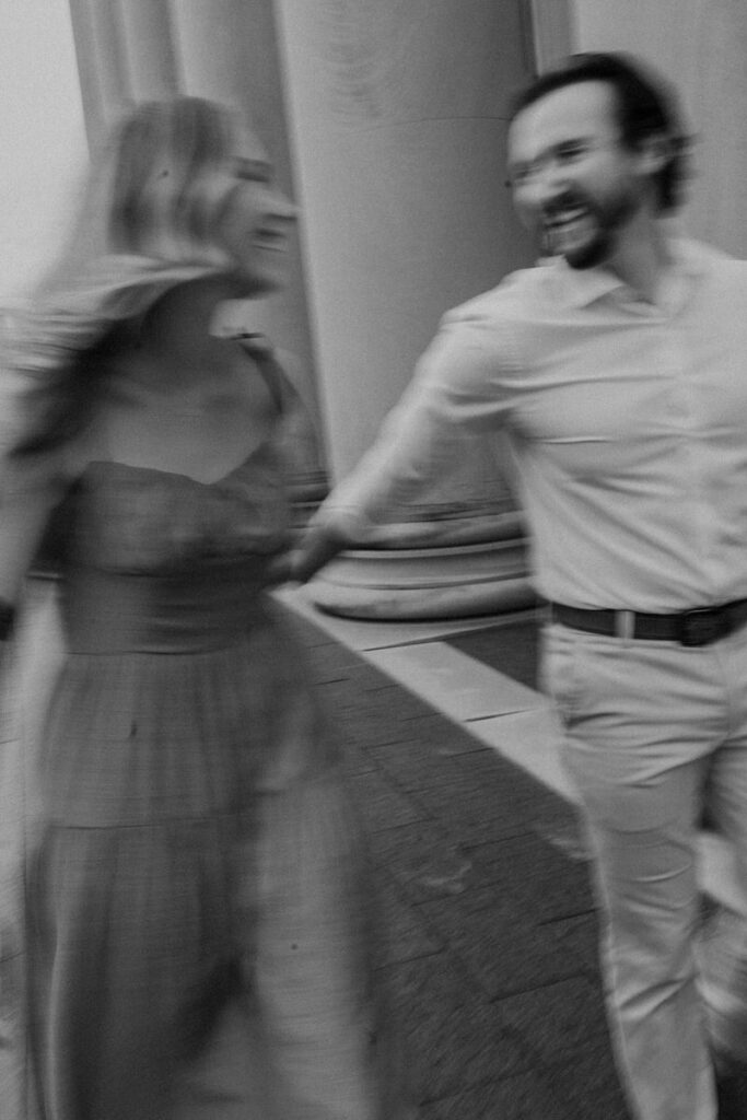 A couple laughing as they swing their hands and walk along a sidewalk