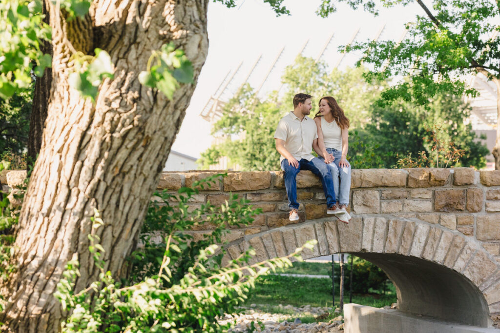 A couple holding hands and sitting the the ledge of a small stone bridge