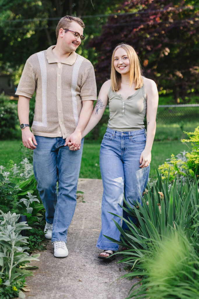 A couple holding hands and smiling while walking in a garden