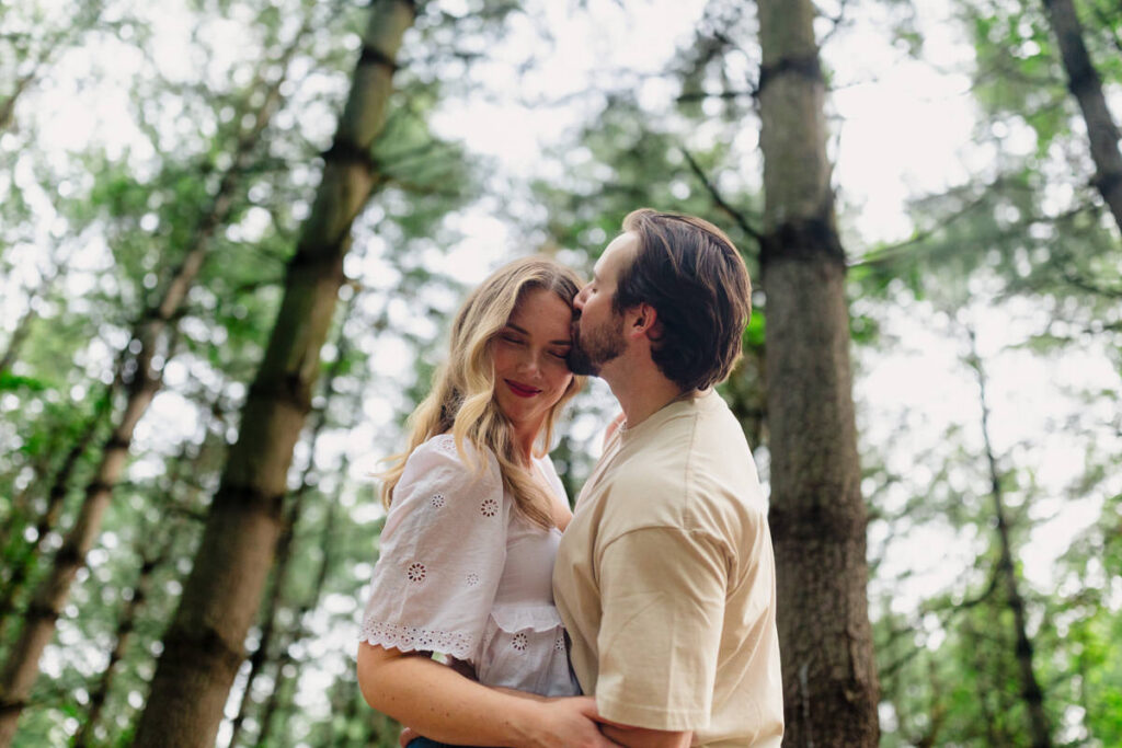 A person smiling as their partner kisses their forehead