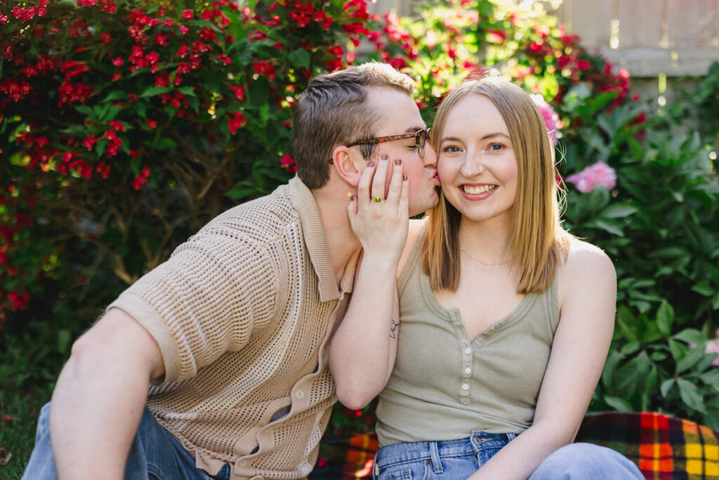 A couple sitting together as one kisses the other's cheek