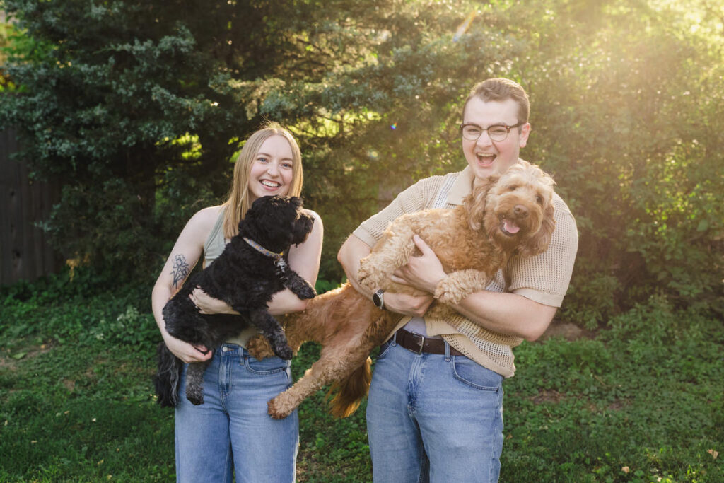 A couple laughing as they both hold dogs