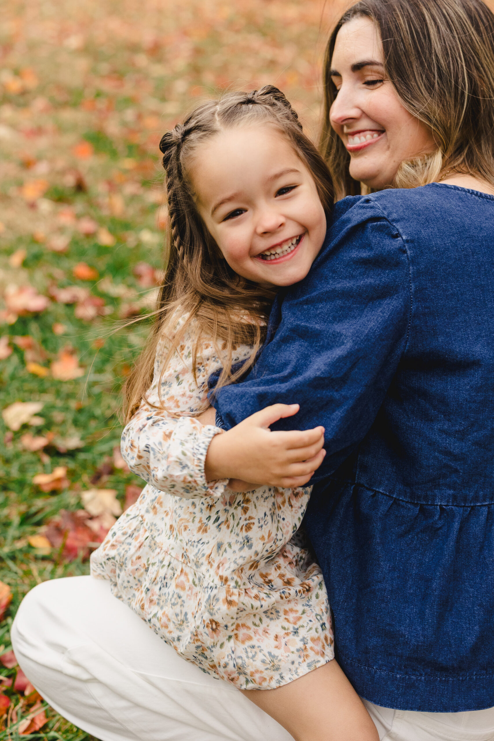 a mother hugging her daughter and sitting on the grass in a park
