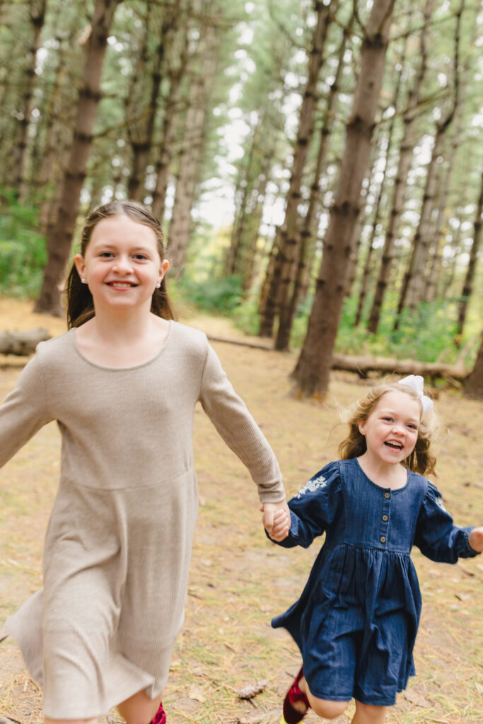 Two young siblings laughing and running in a wooded area 