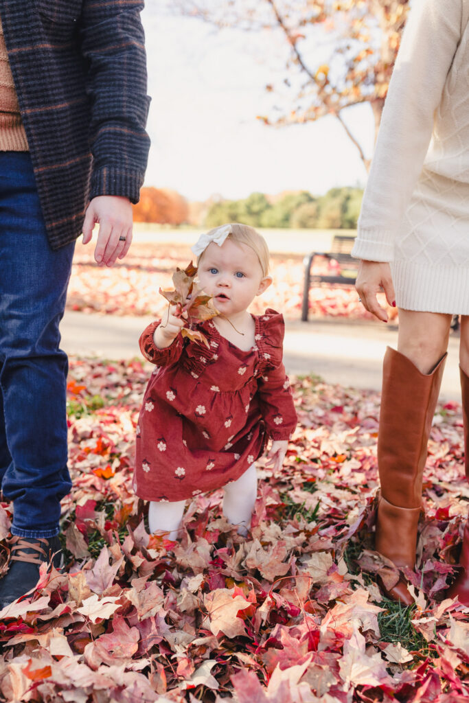 A toddler holding up a leaf with their parents on either side 