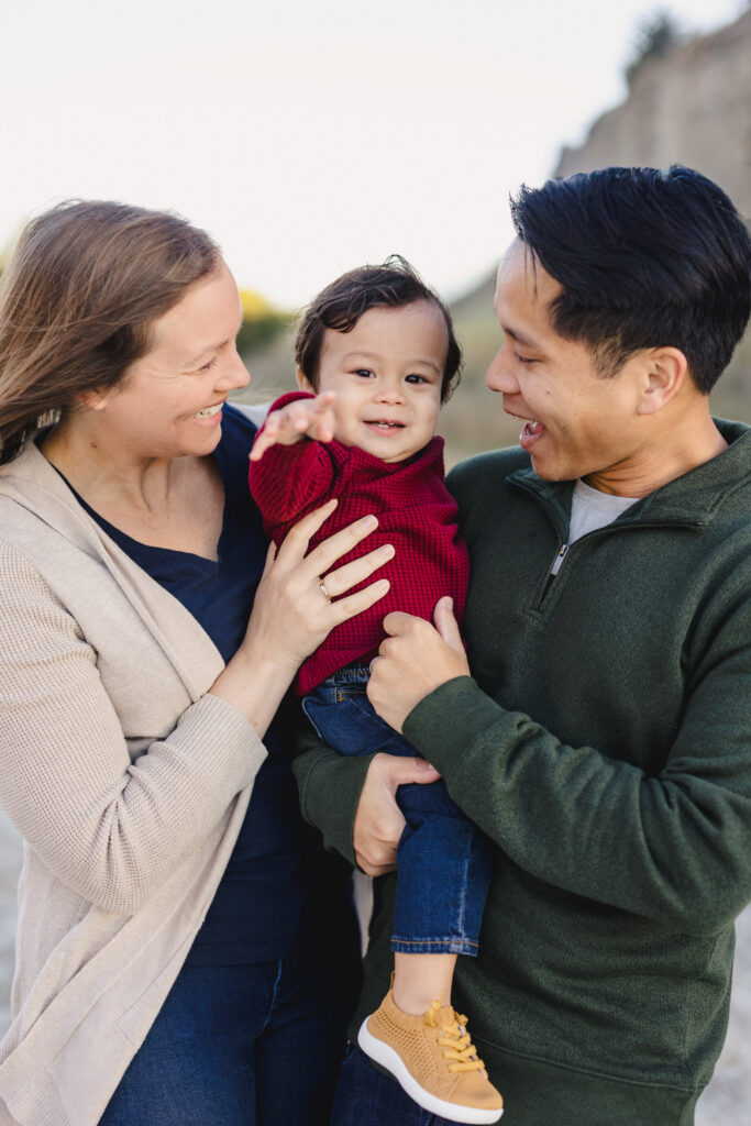 Parents holding their toddler between them as they laugh together 