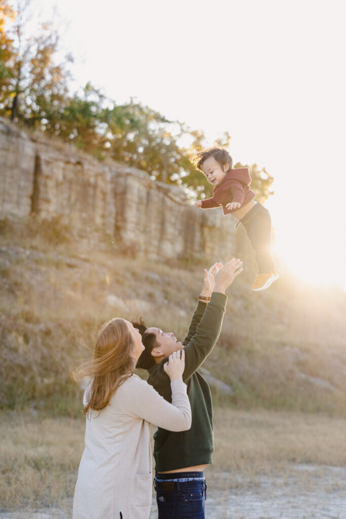 Parents standing on a beach while one throws their toddler in the air 
