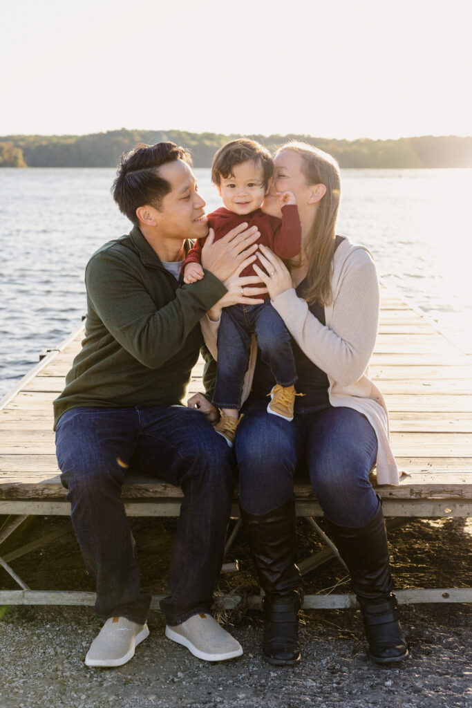 Parents sitting on a pier while they hold their child between them 