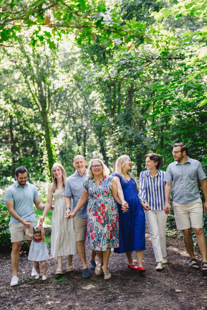 An extended family walking together along a path in a wooded area as they all laugh 