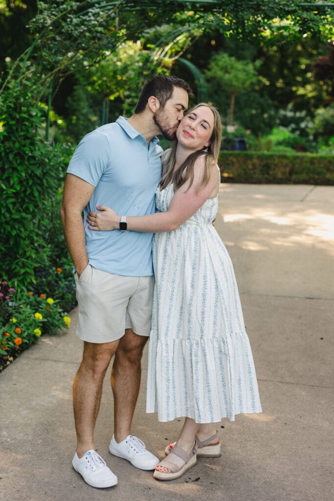 A person kissing their partner's cheek as they stand in a garden 
