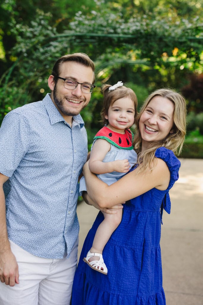 A couple smiling while holding a toddler between them 