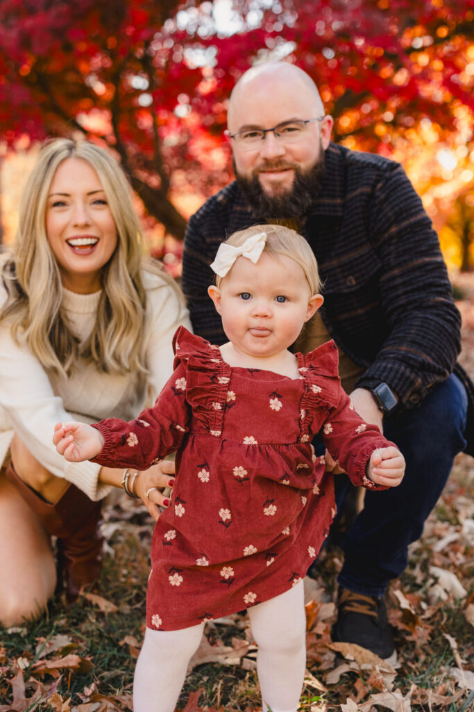 Parents squatting behind their child as they walk in a field 