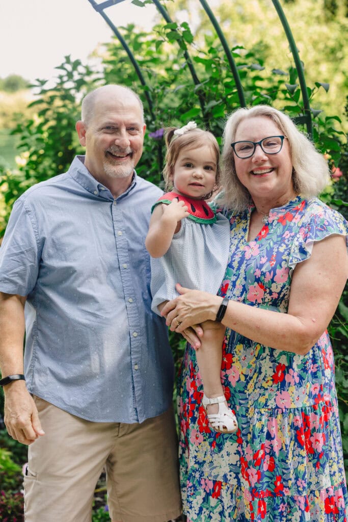 Grandparents smiling as they hold their grandchild between them 