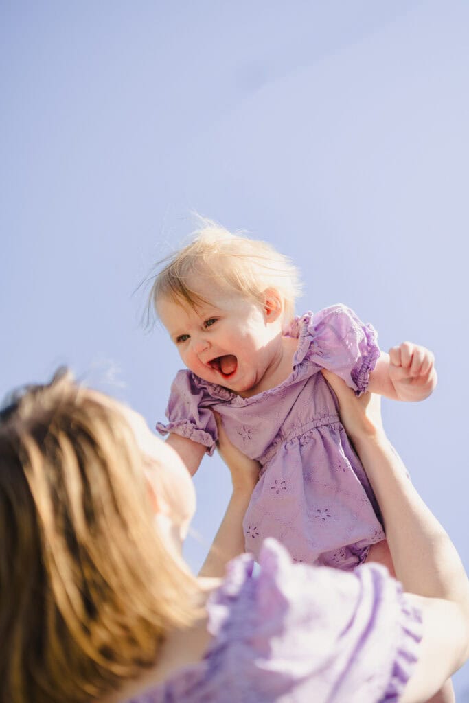 A parent holding up their toddler in the air as they laugh 