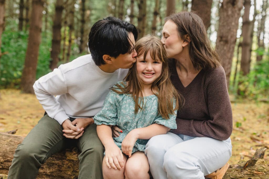 A child sitting in between their parents as they both kiss their forehead 