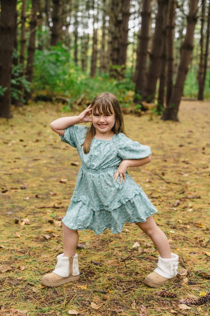 A child smiling and posing with one hand on their head and the other on their hip 
