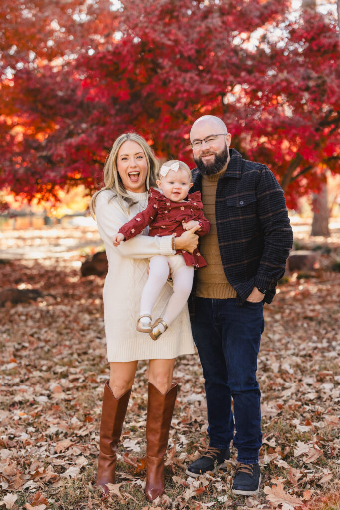Parents smiling together in a park as one holds their toddler 