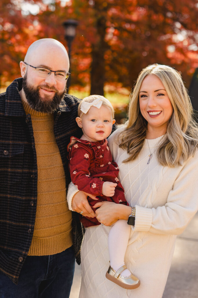 A parent holding their child on their hip with their partner standing next to them 
