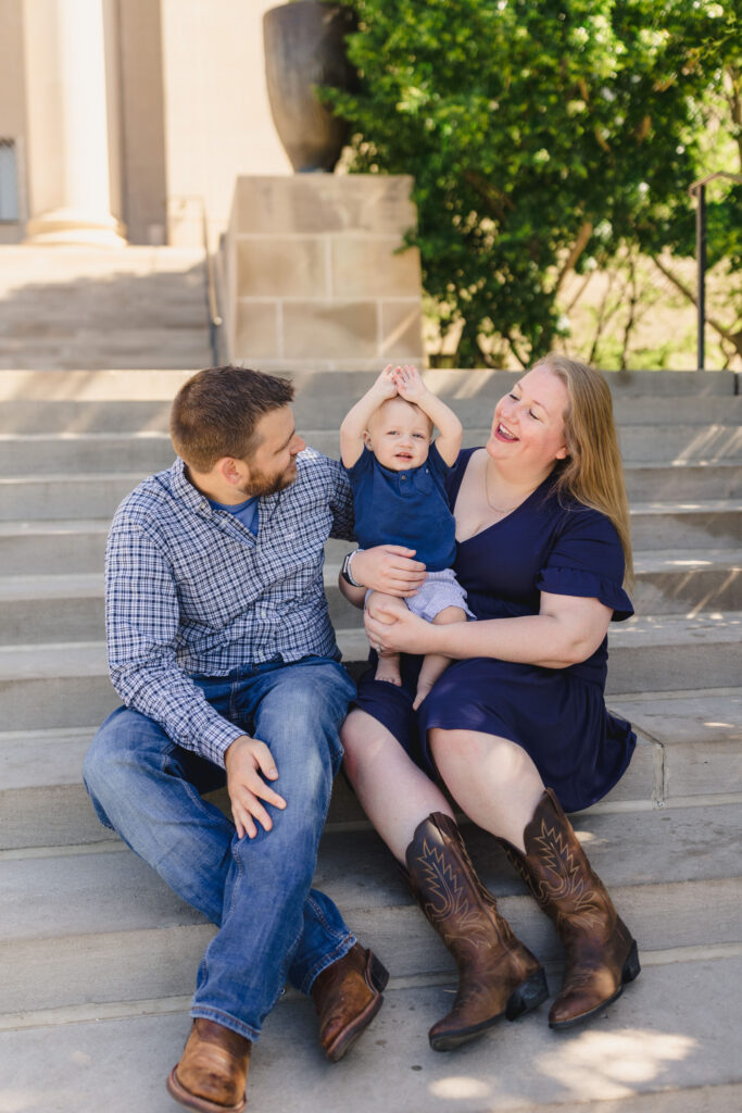 Parents sitting on steps with their toddler between them with their hands in the air 