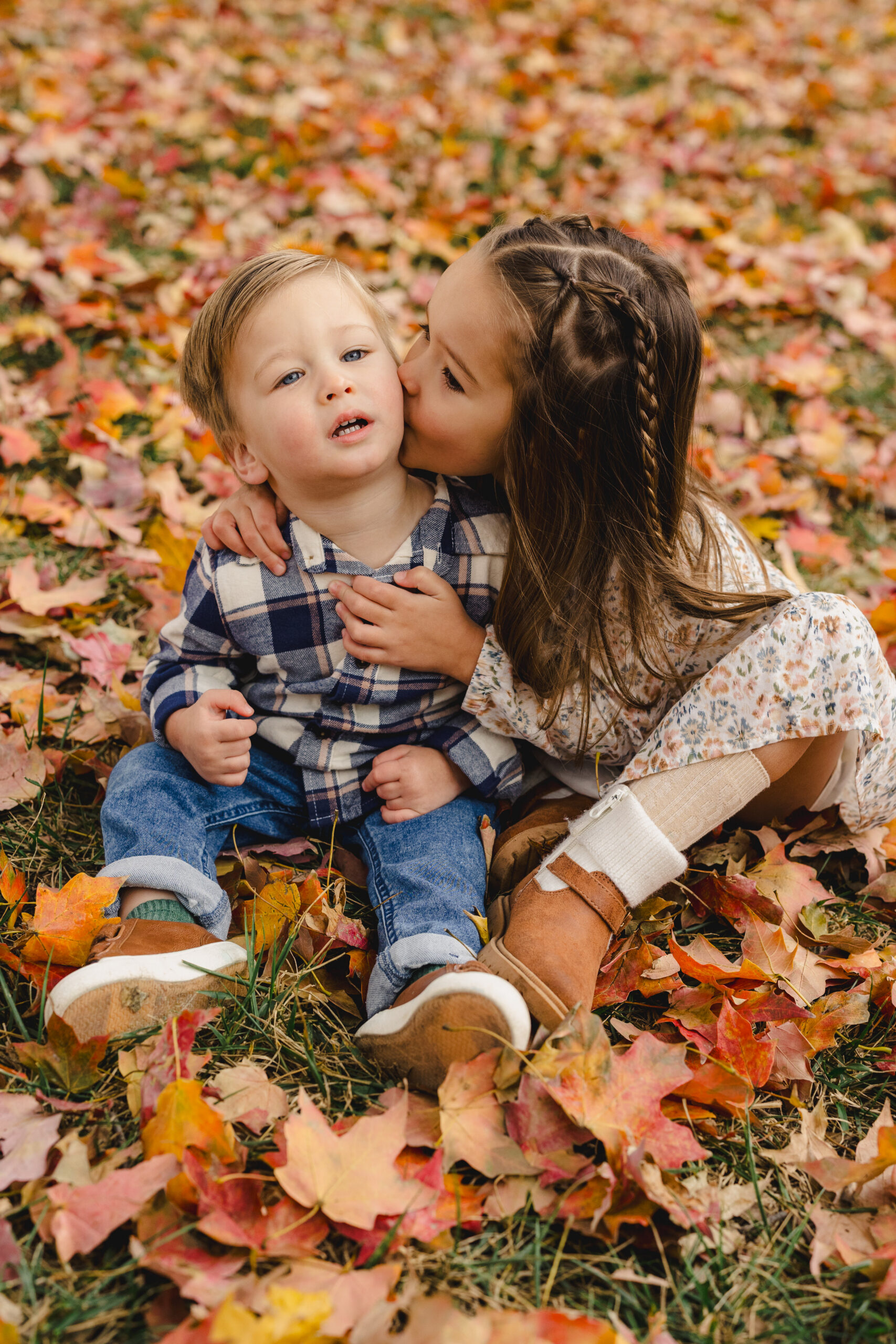 a brother and sister sitting in the fall leaves taking family photos 