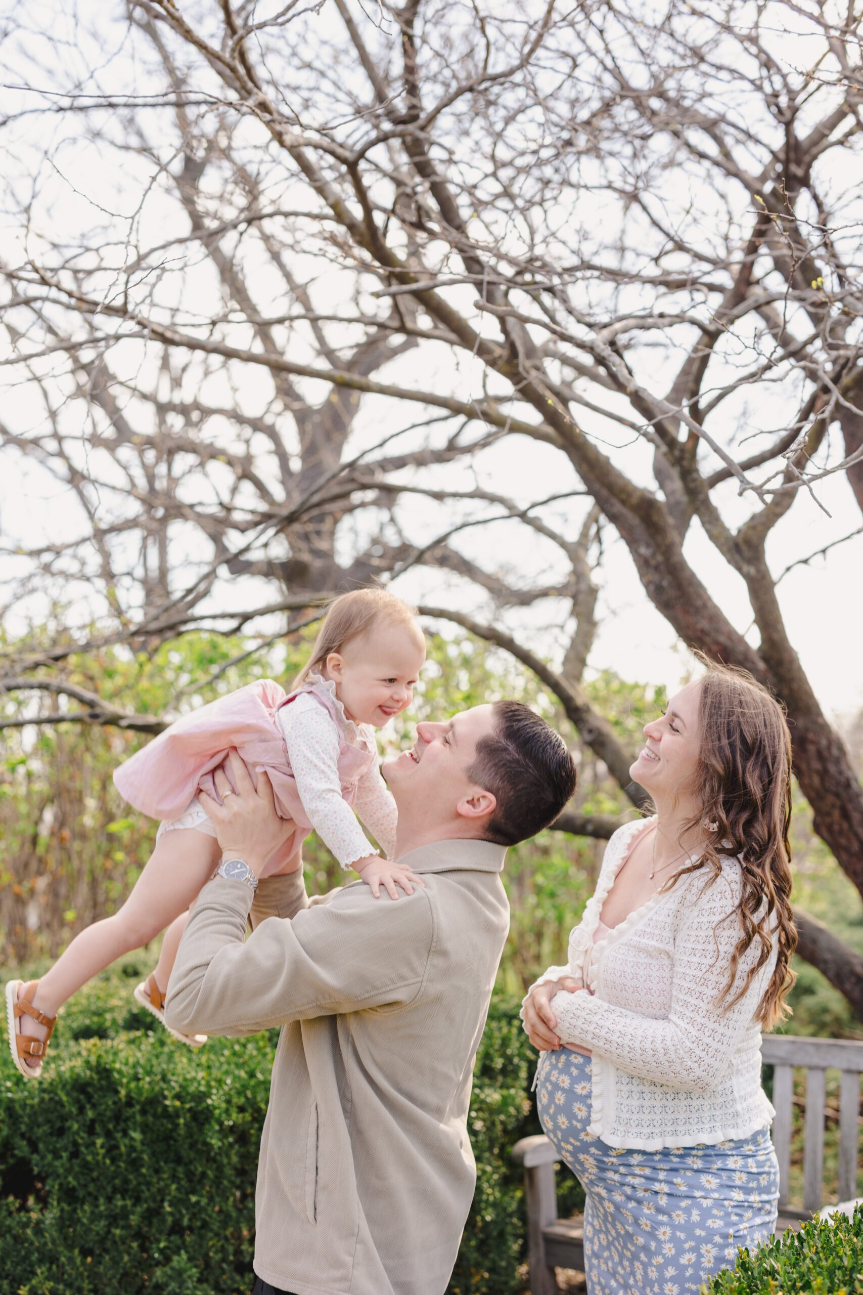 a mother, father, and their daughter the father is holding his daughter up in the air