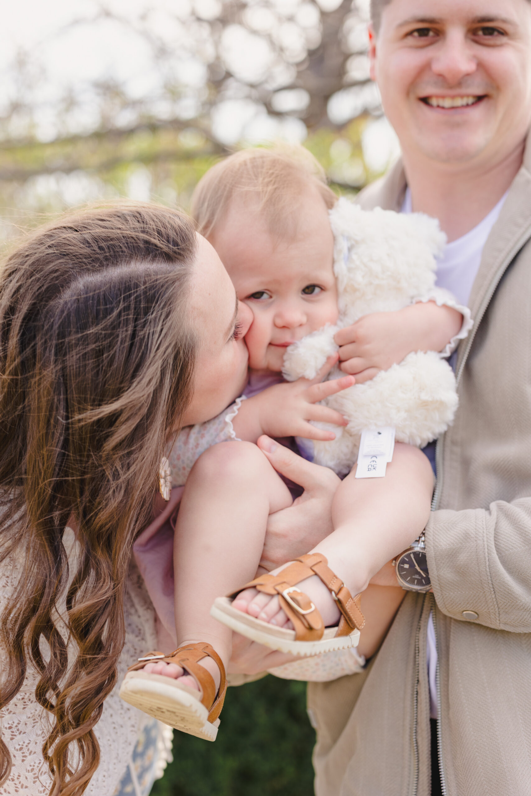 a mother giving her daughter a kiss on the cheek while her father holds her 